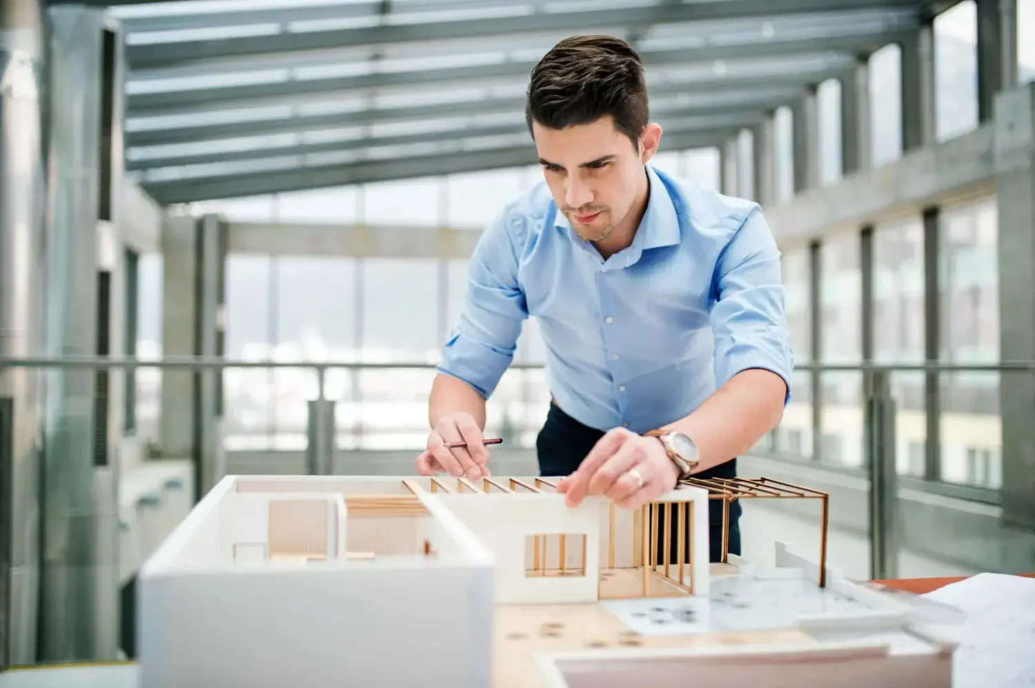 Junger Geschäftsmann oder Architekt mit Hausmodell steht im Büro und arbeitet.